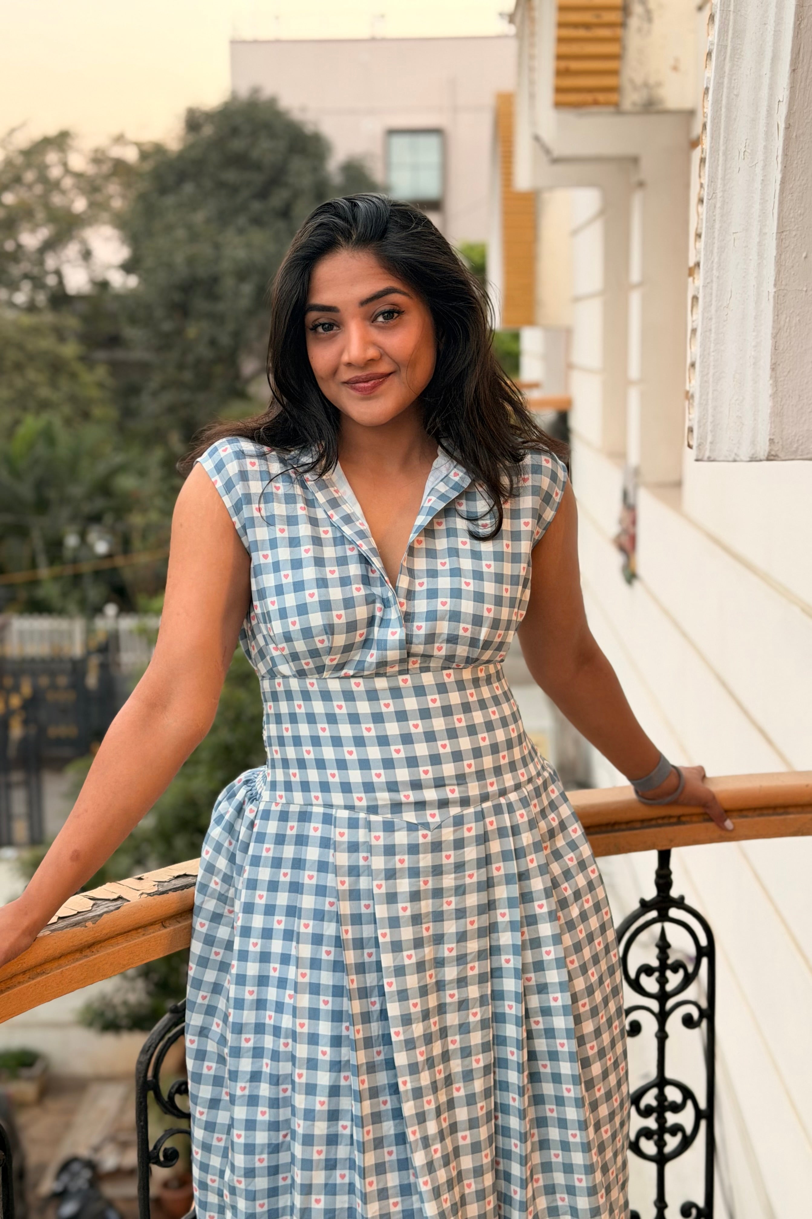Woman in a checkered dress standing on a balcony with a blurred background