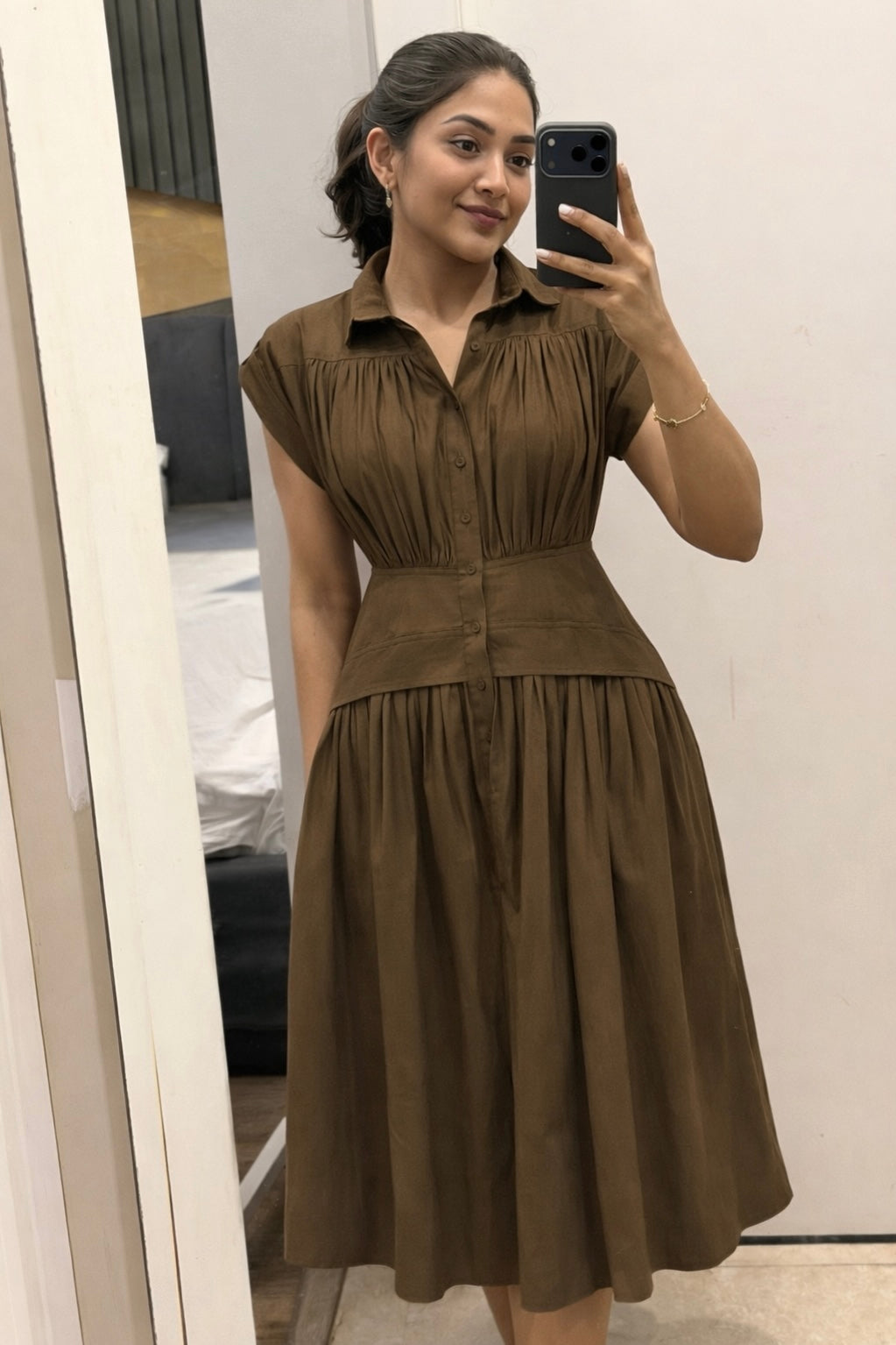 Woman wearing a brown dress taking a mirror selfie.