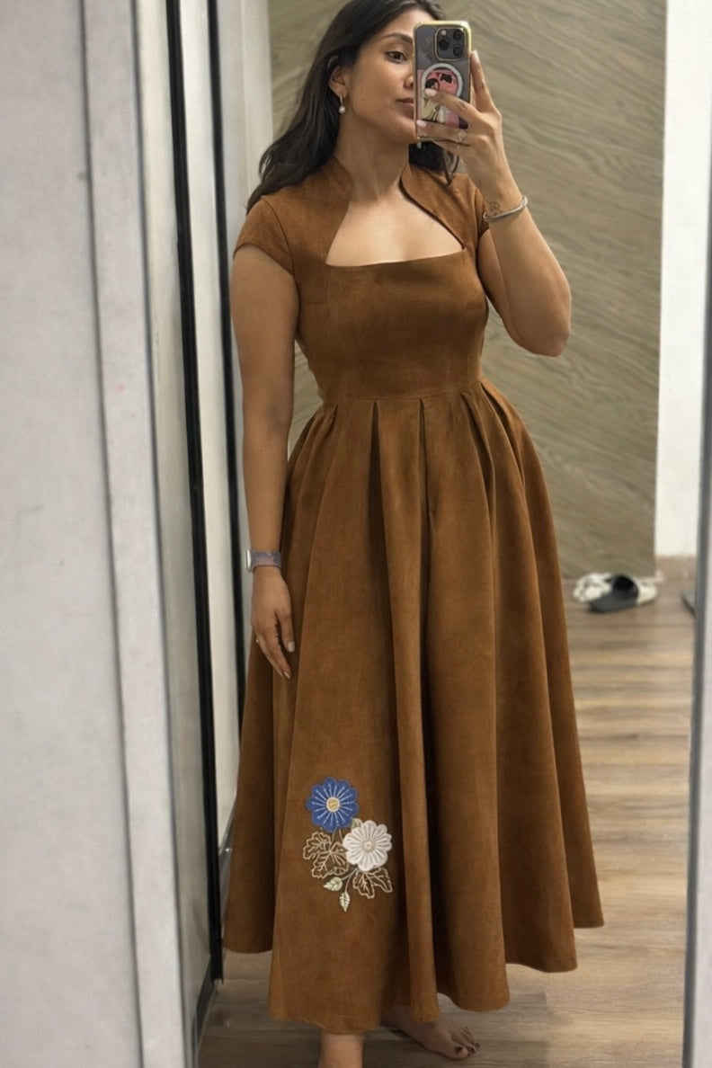 Woman wearing a brown dress with floral embroidery, standing in front of a mirror.