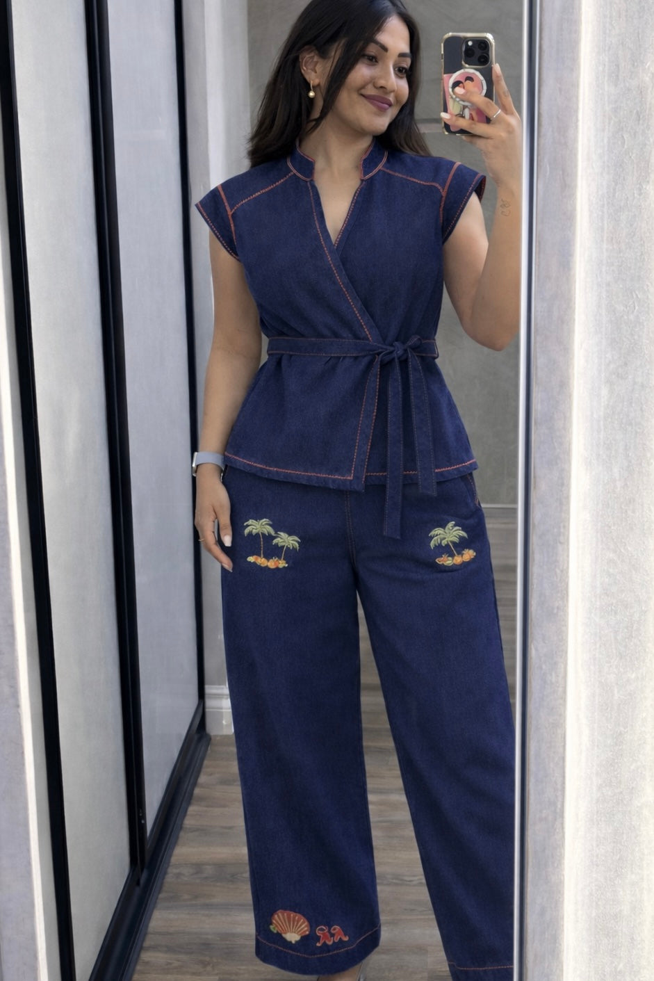 Woman wearing a navy blue jumpsuit with palm tree and shell designs, standing in front of a mirror.
