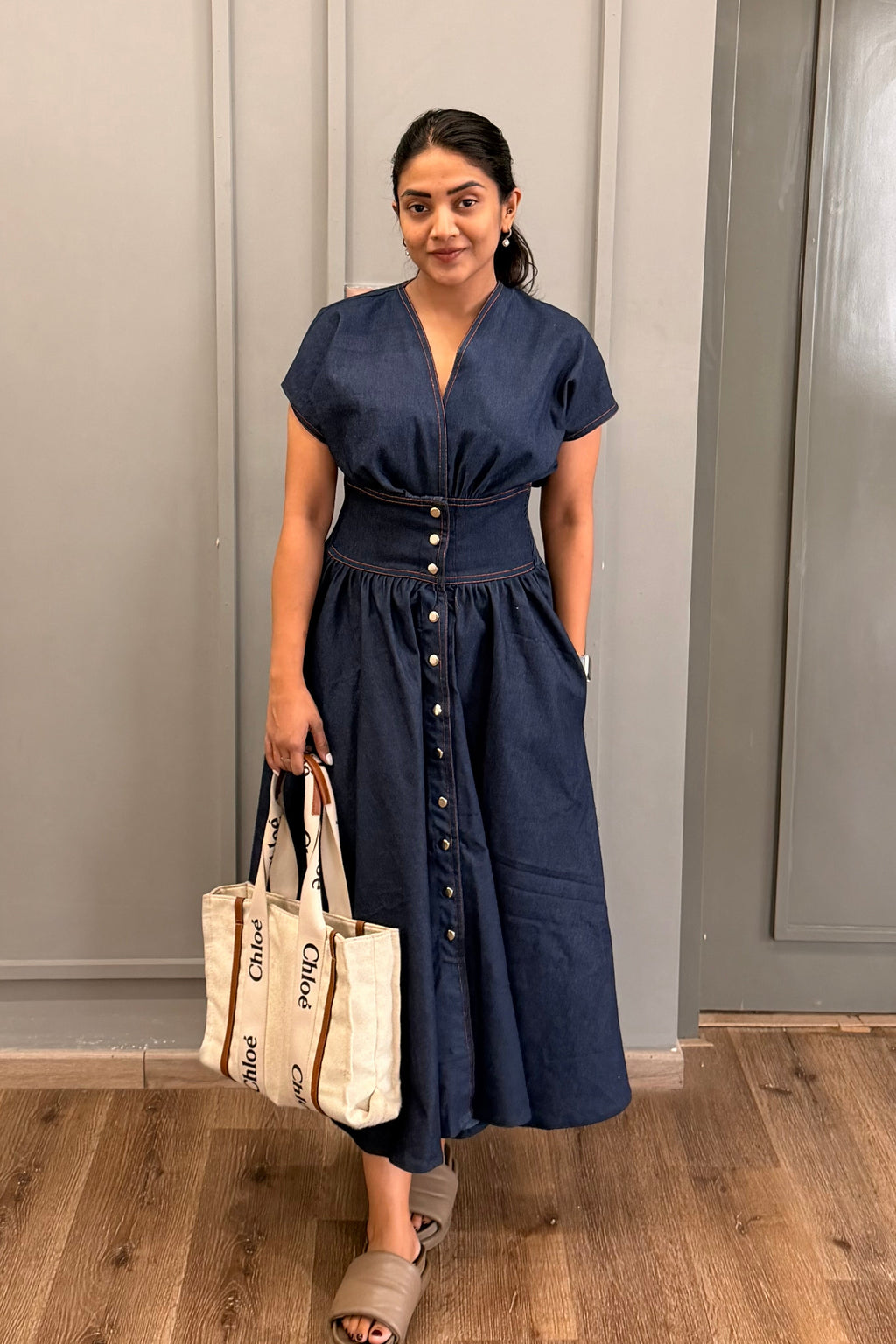 Woman in a comfortable denim midi navy dress holding bags in a room 