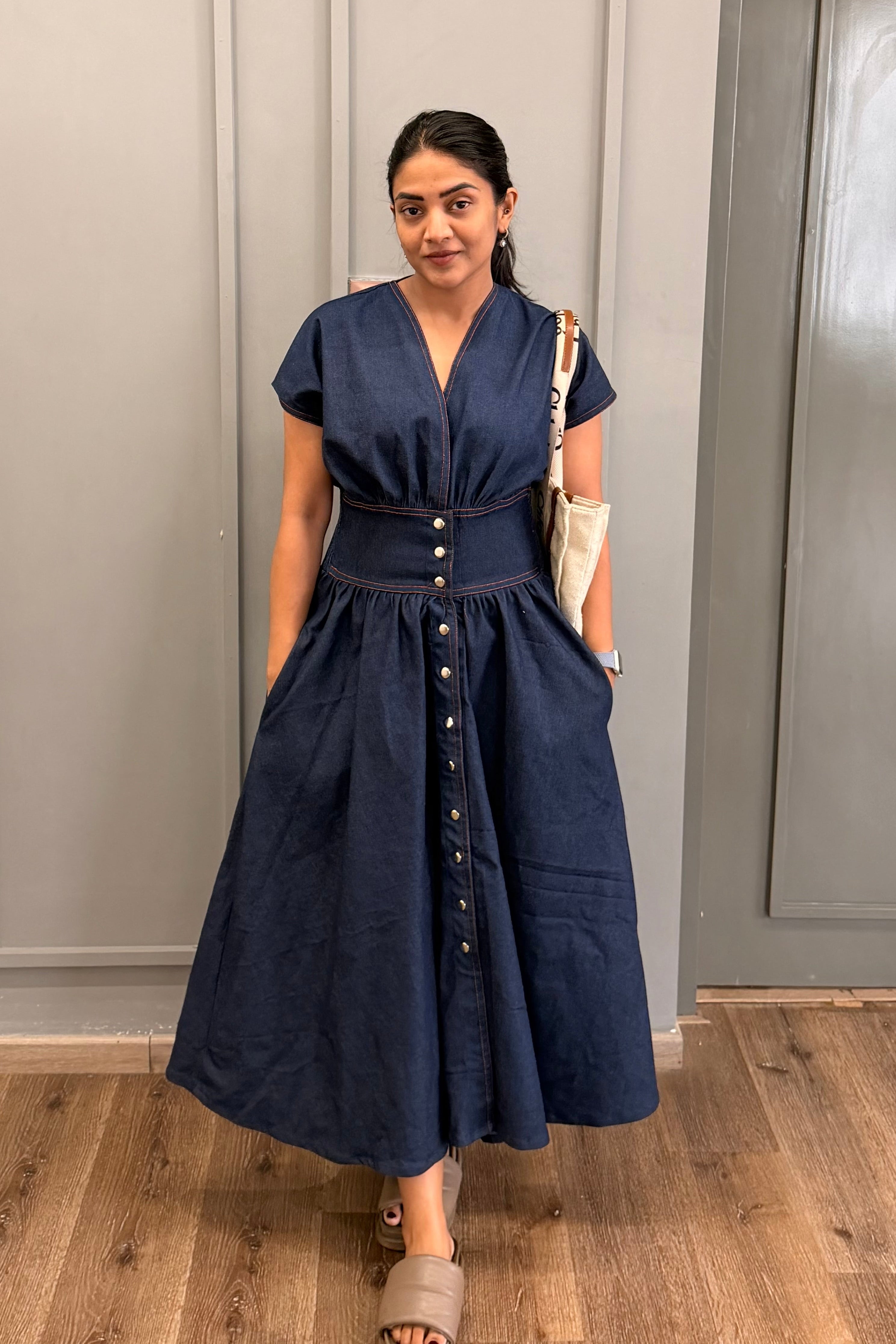 Woman wearing a blue dress standing in a room with gray walls and wooden flooring.