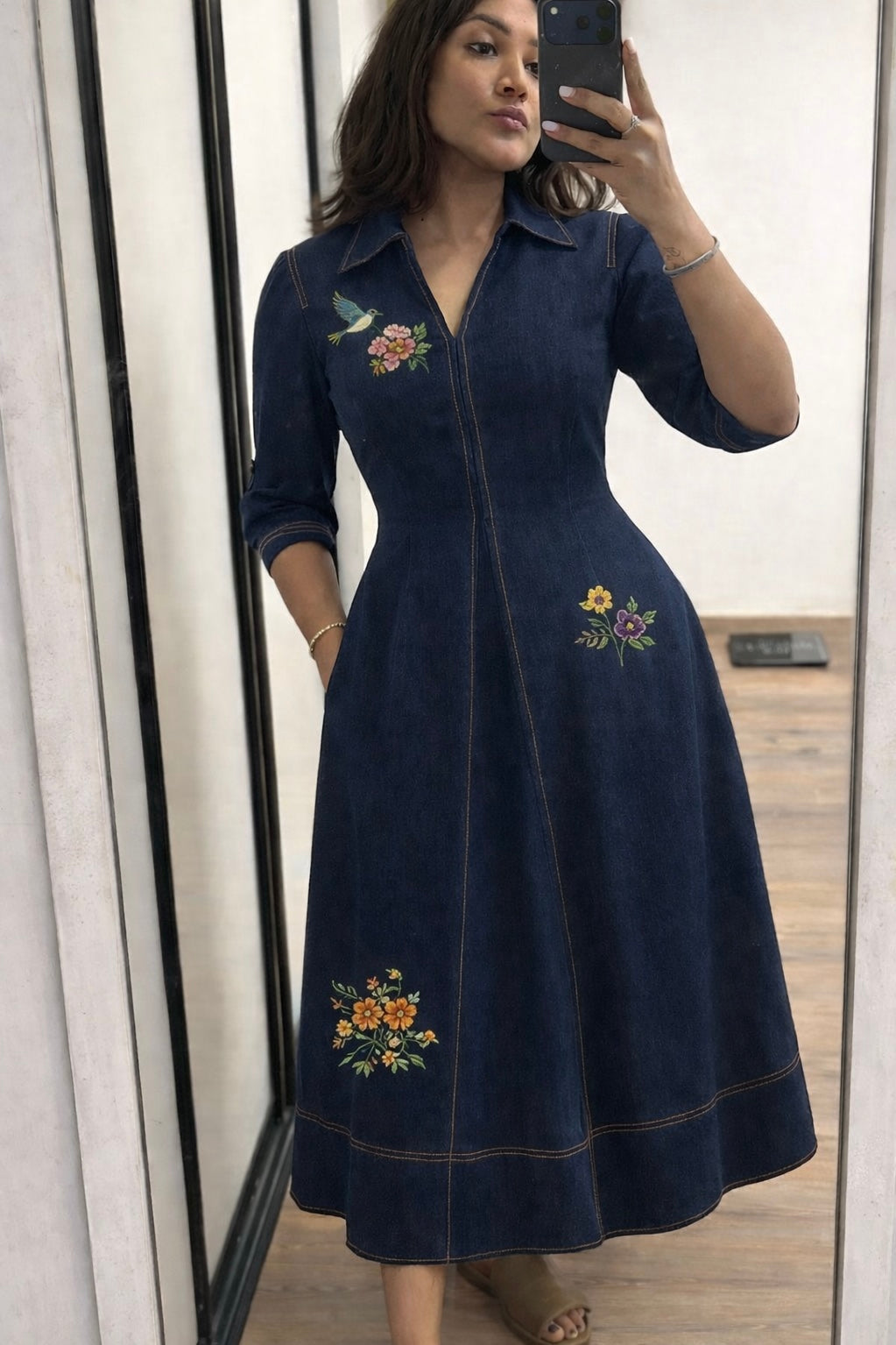 Woman wearing a navy dress with floral embroidery in front of a mirror.