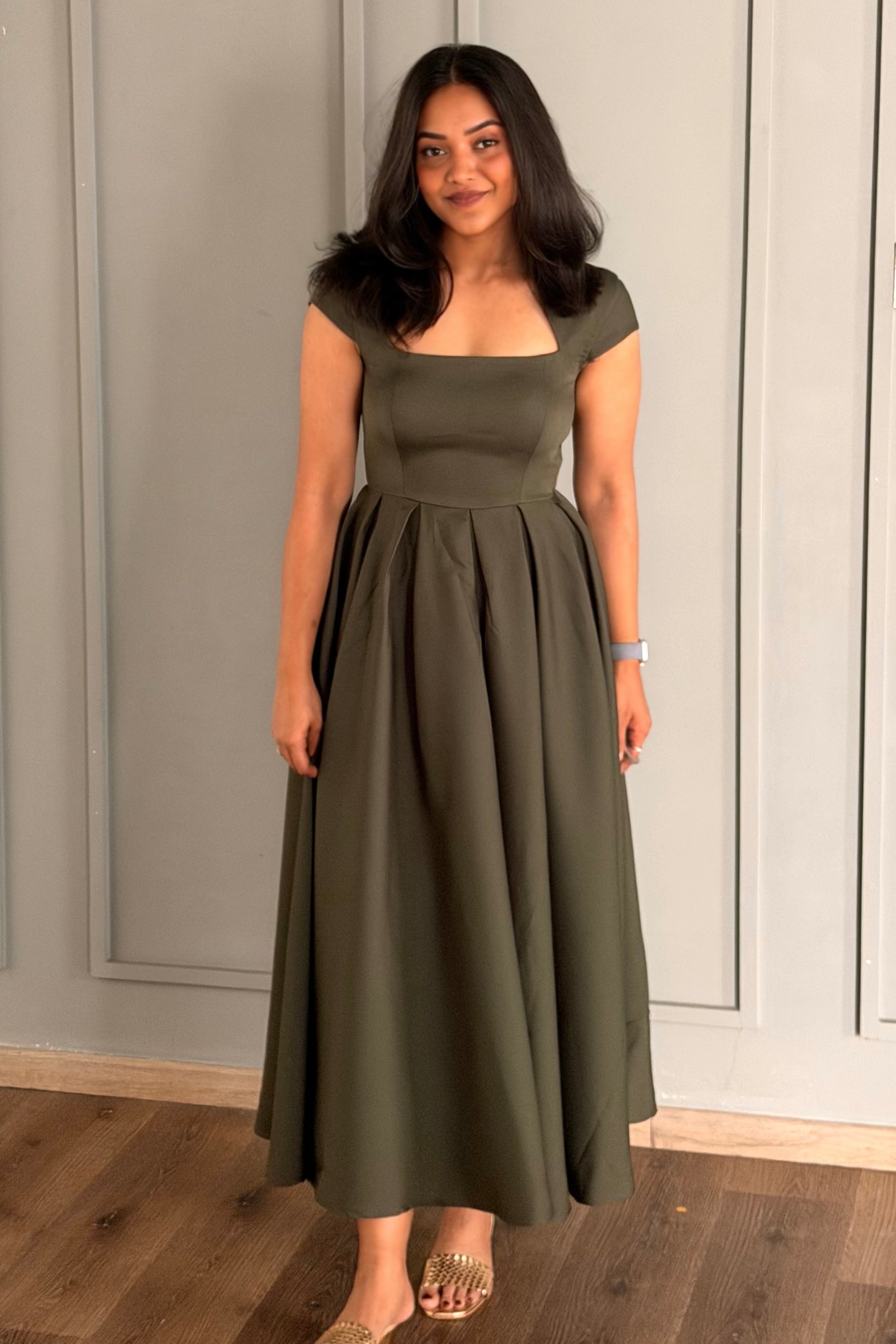 Woman wearing an olive green dress standing against a neutral wall.