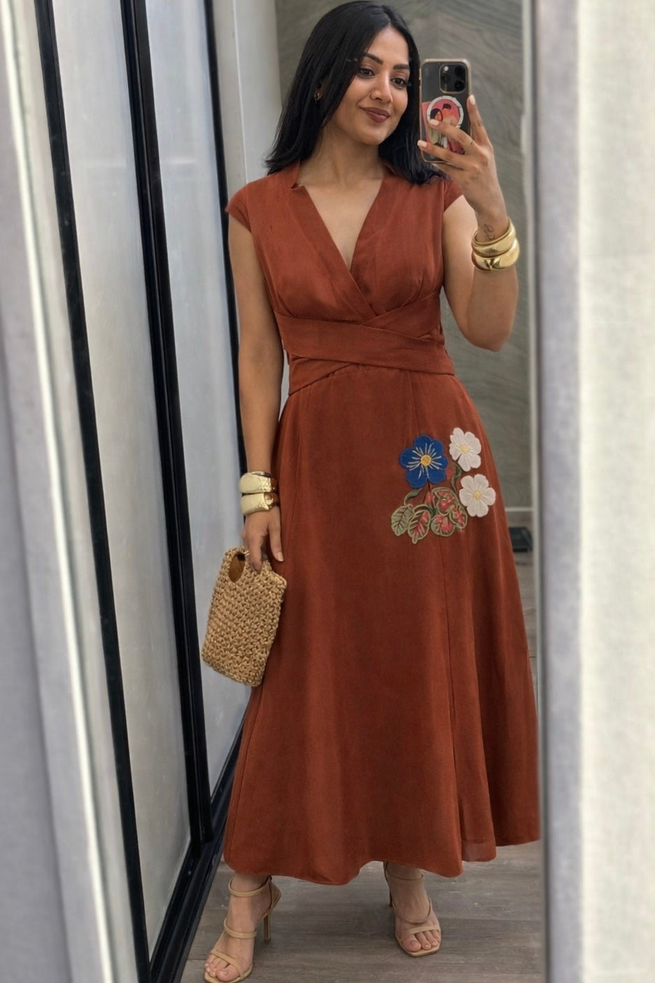 Woman in a brown dress with floral embroidery standing in front of a mirror.