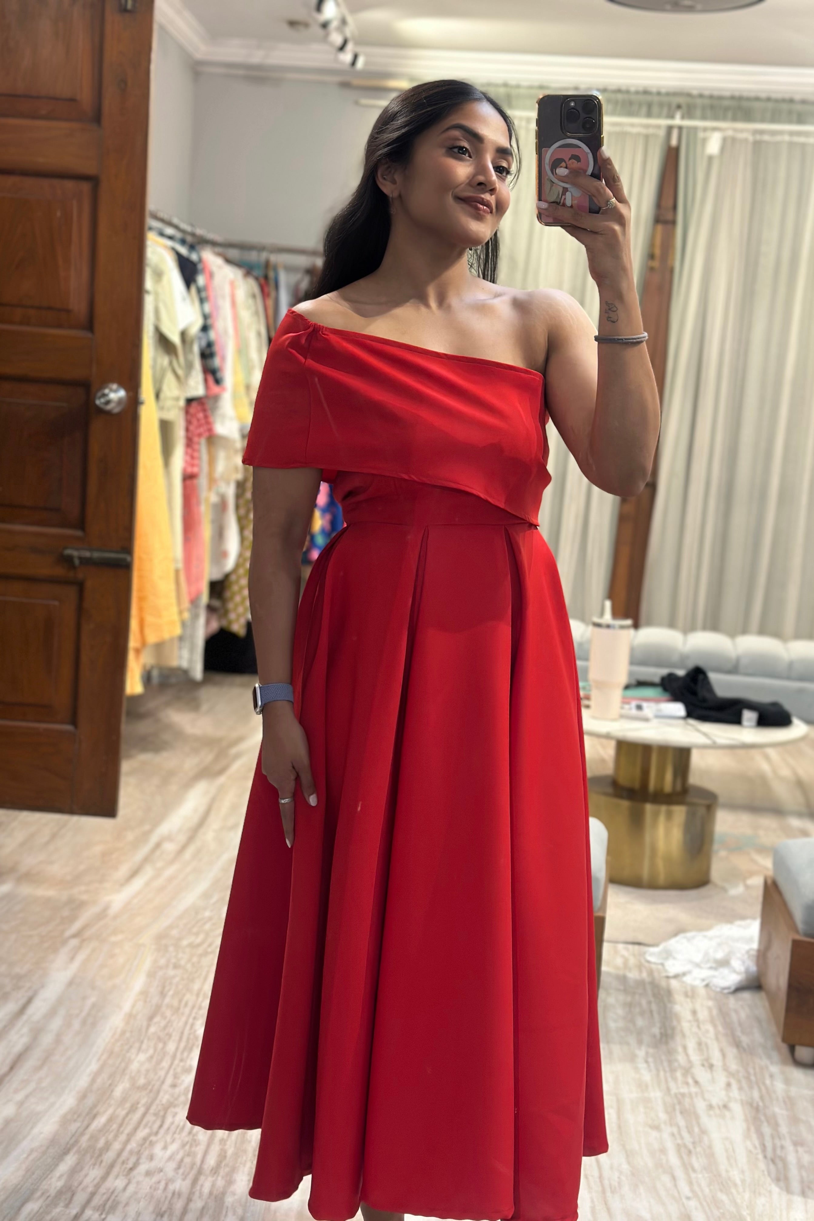 Woman wearing a red one-shoulder dress in a room with wooden floor and clothing racks.