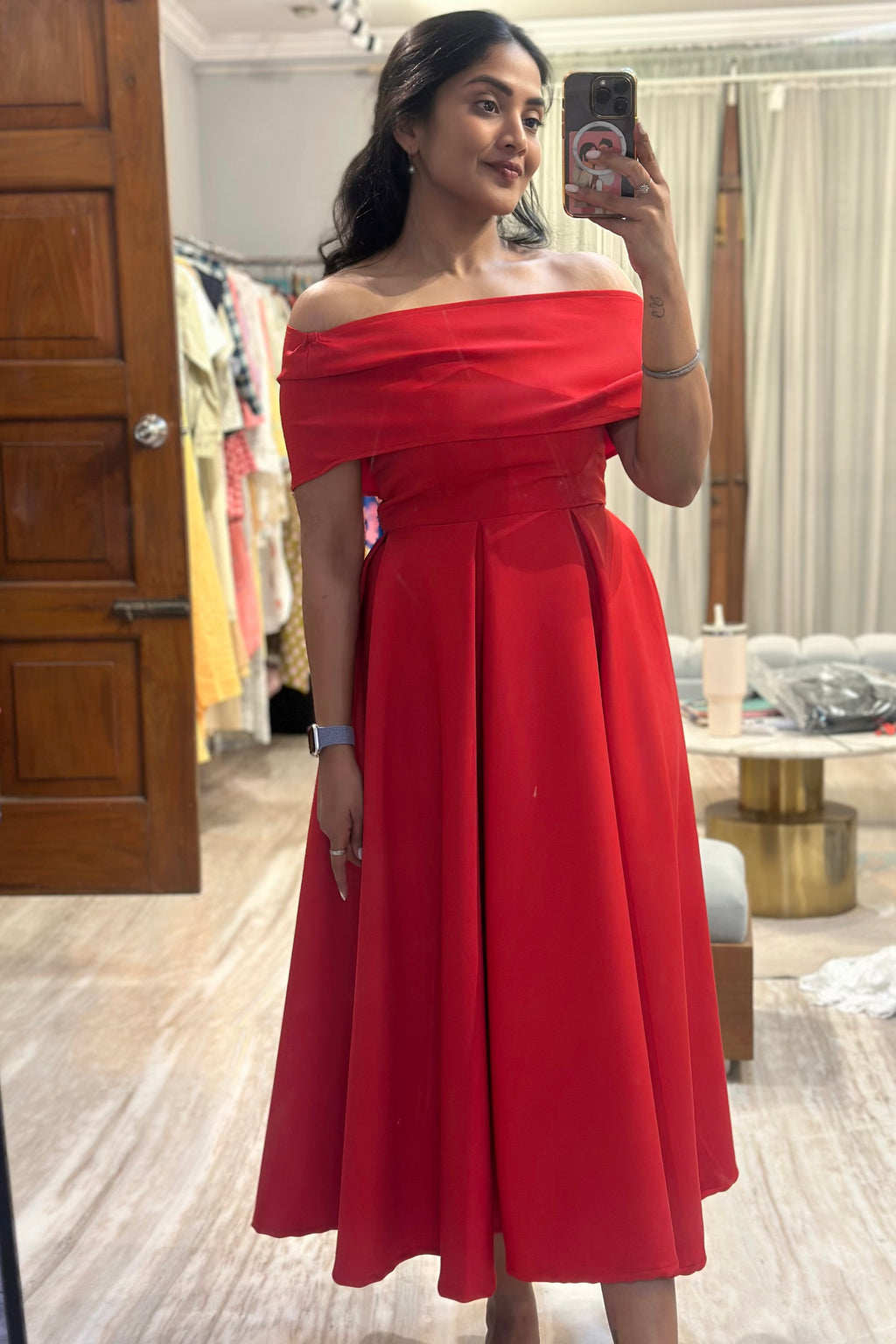 Woman wearing a red off-shoulder dress taking a mirror selfie.