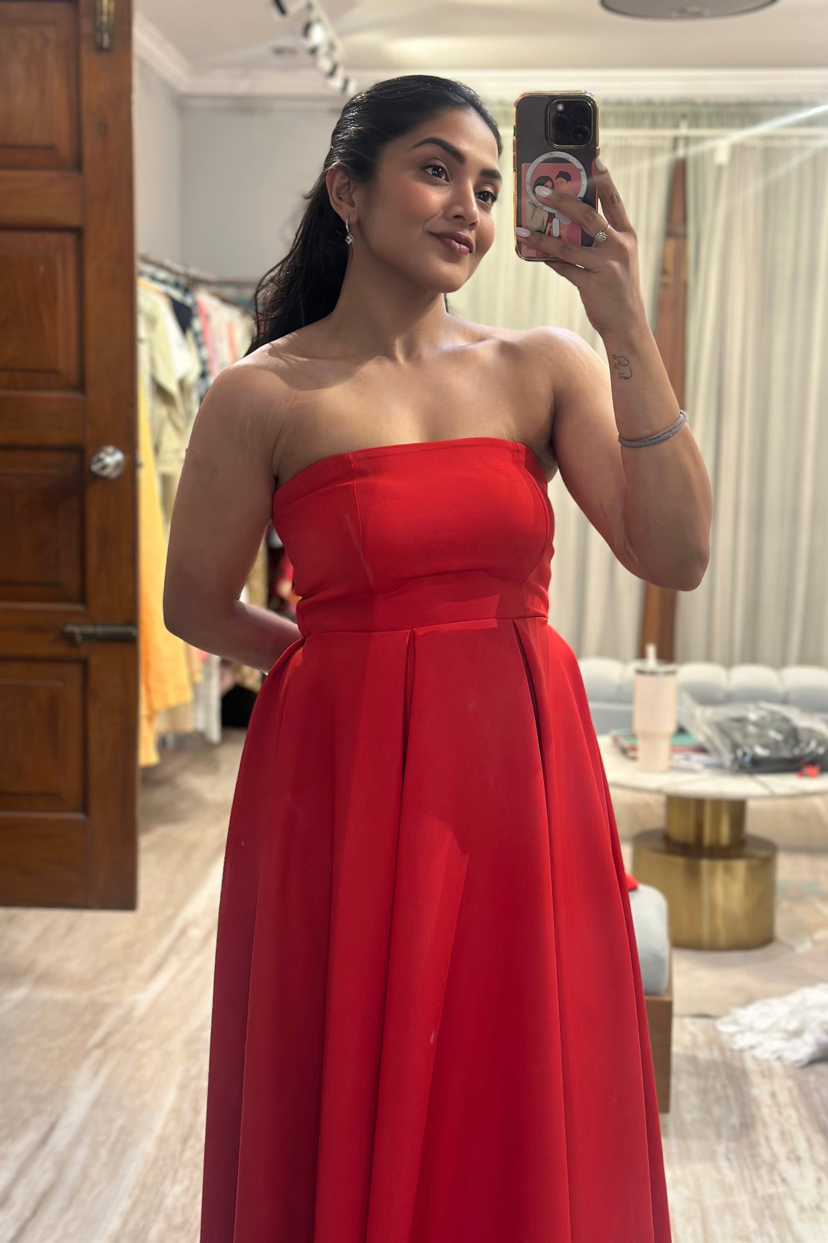 Woman in a red strapless dress taking a mirror selfie in a room.