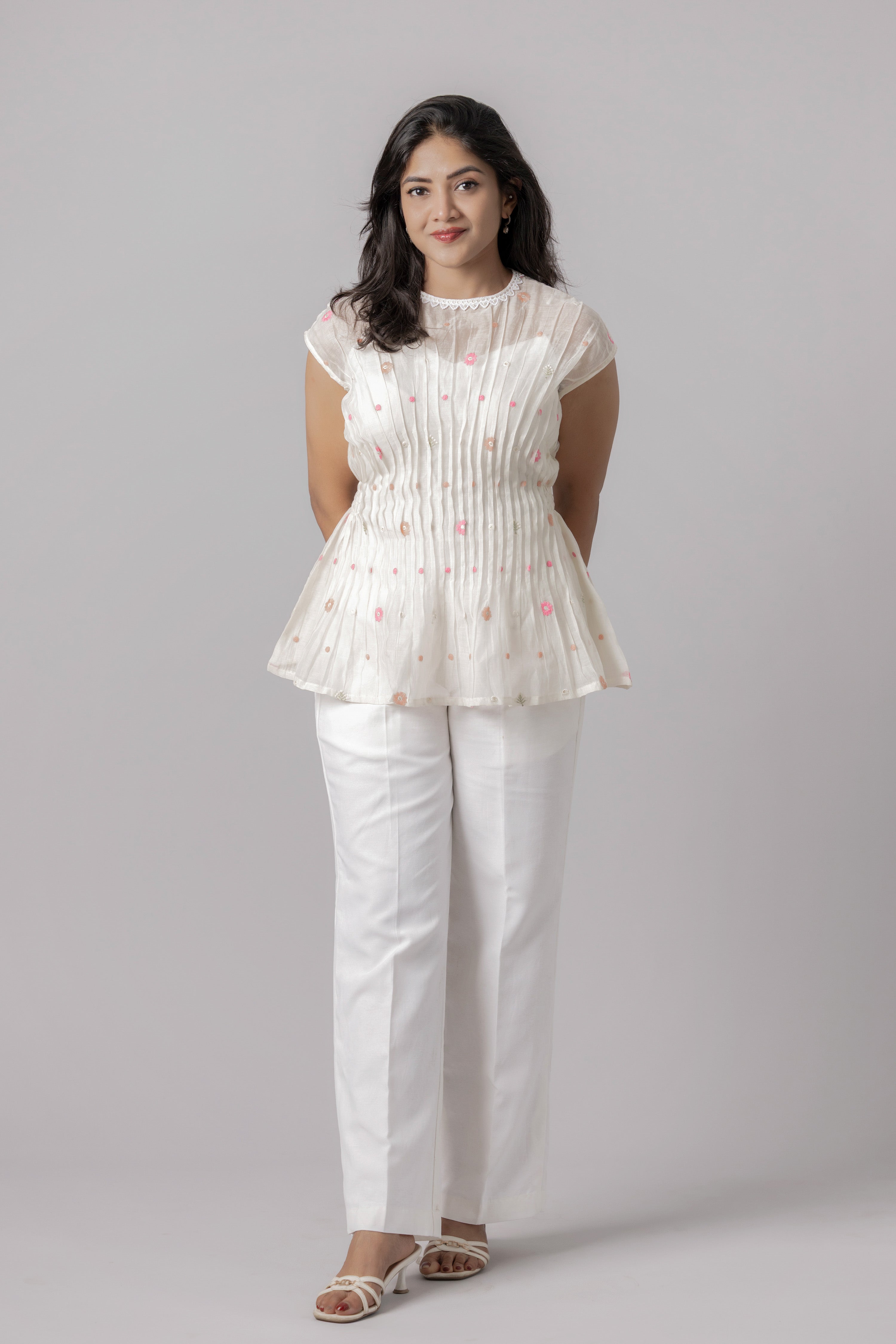 Woman wearing a white embroidered sheer peplum top with pleated detailing.