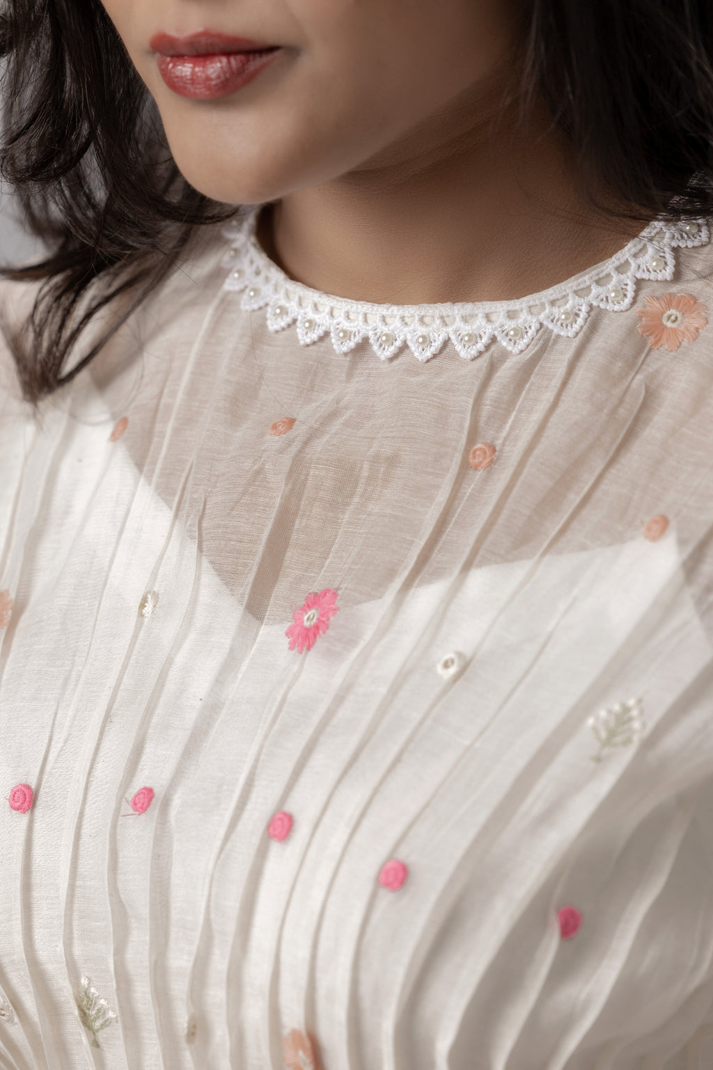 Woman wearing a white embroidered sheer peplum top with pleated detailing.