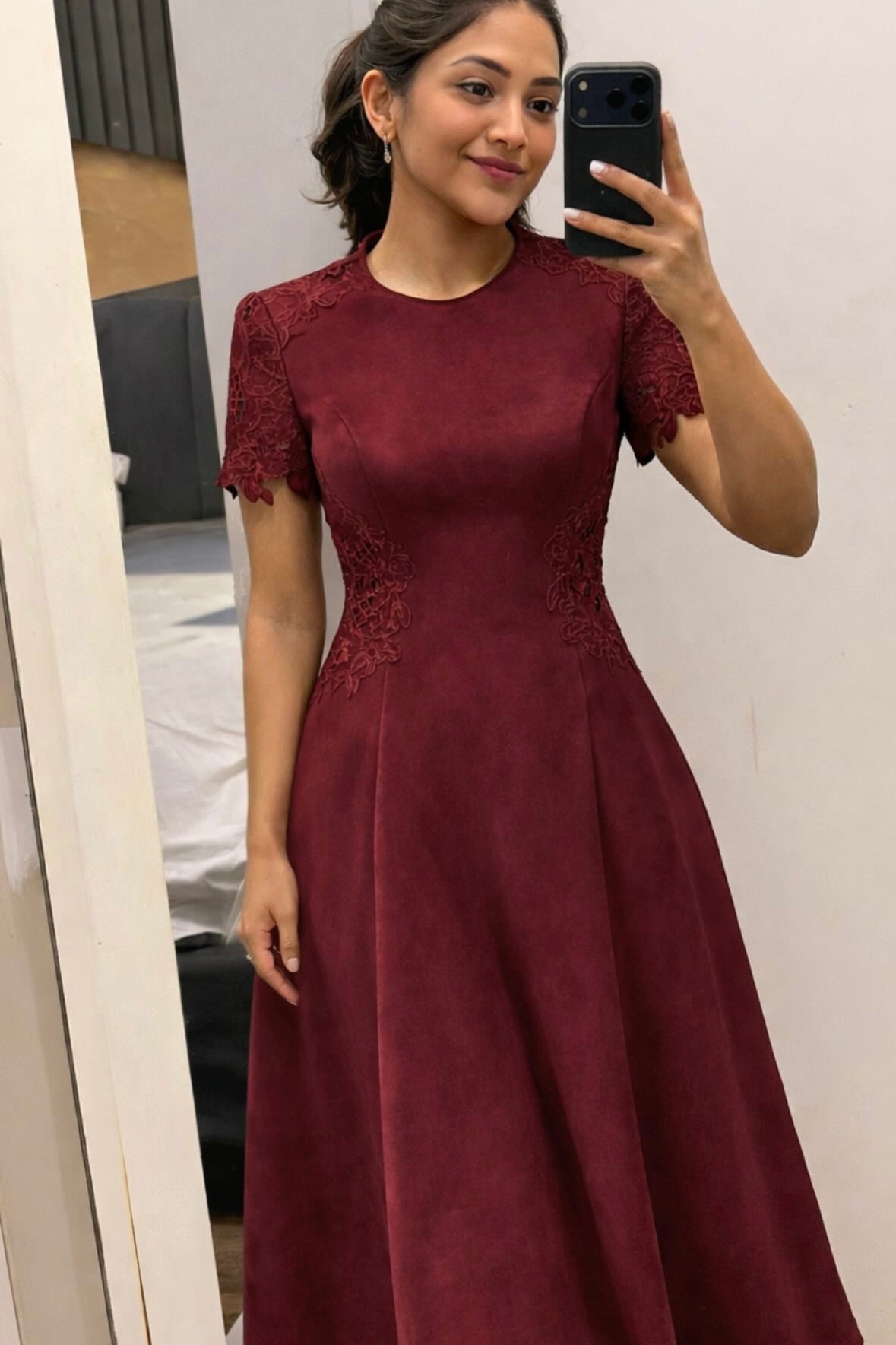 Woman wearing a burgundy dress with lace details, taking a mirror selfie.